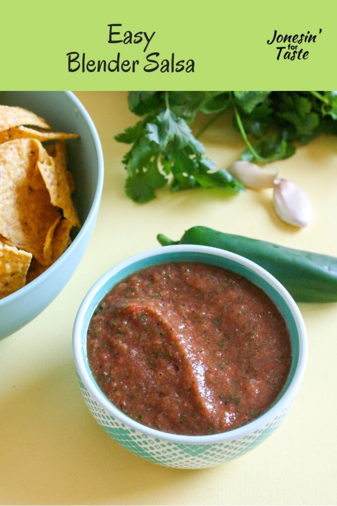 A bowl of salsa on a table with cilantro, garlic, and jalapeno