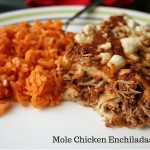 Two mole enchiladas cut in half on a plate next to Mexican rice