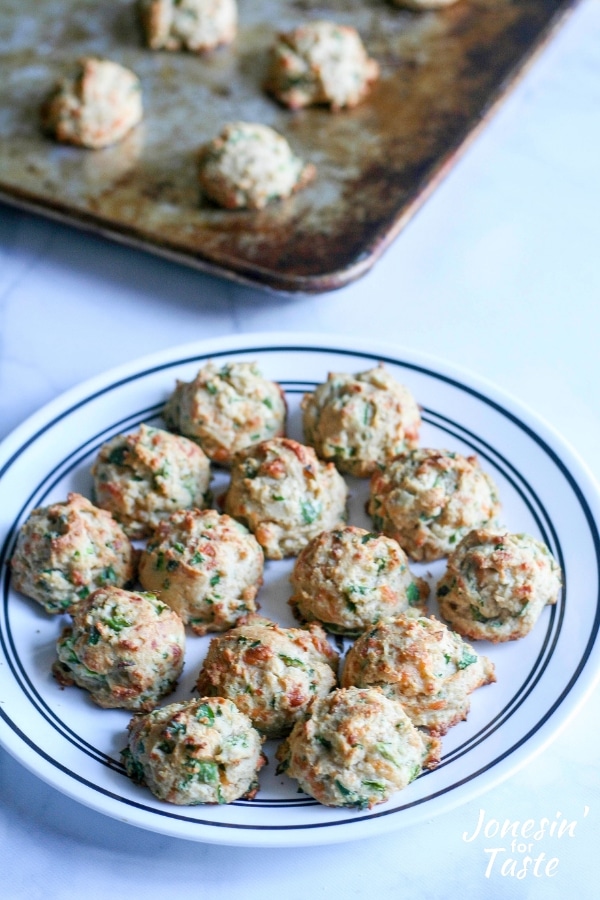 A plate of cheesy garlic jalapeno drop biscuits next to a cookie sheet of baked biscuits
