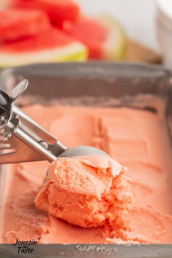 an ice cream scoop being used to scrape a scoop of the pink-orange ice cream from a loaf pan
