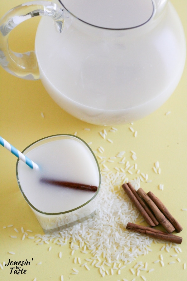 A glass of horchata next to rice, cinnamon sticks, and a pitcher