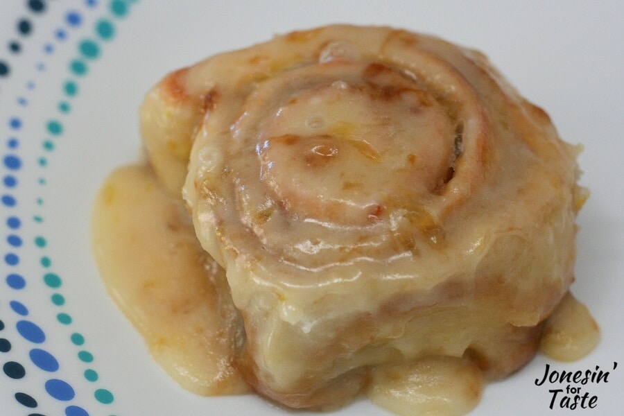 One of the quick no-yeast Orange Rolls on a plate dripping with orange glaze.