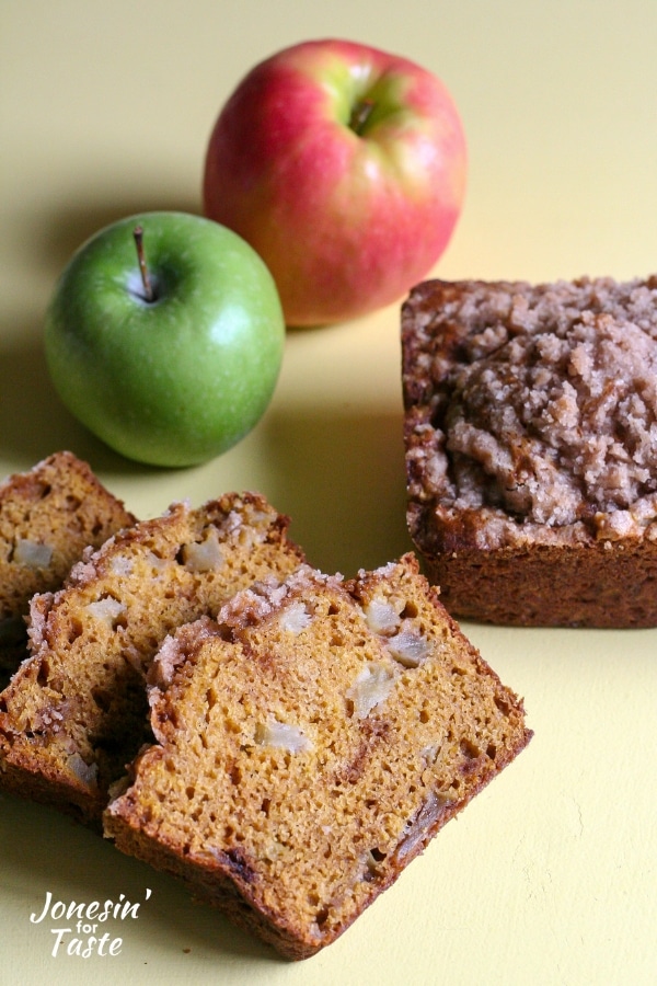 Slices of pumpkin apple bread next to a loaf and apples