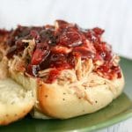 A Slow Cooker Cranberry Chicken on an onion roll topped with cranberry BBQ sauce.