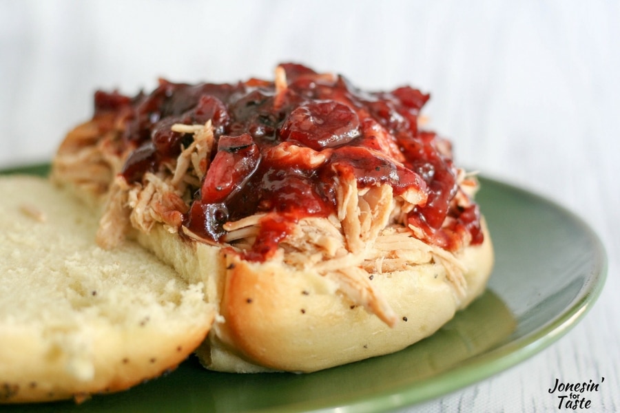 A Slow Cooker Cranberry Chicken on an onion roll topped with cranberry BBQ sauce.