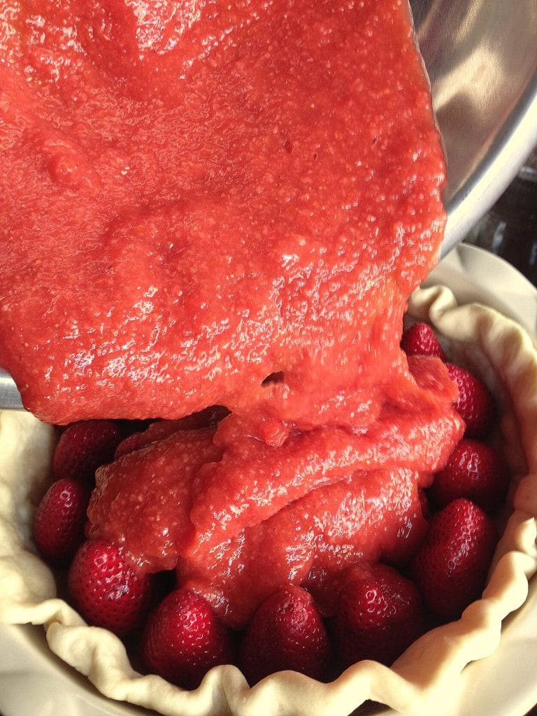 Homemade strawberry puree being poured over whole strawberries for this No Bake Fresh Strawberry Pie
