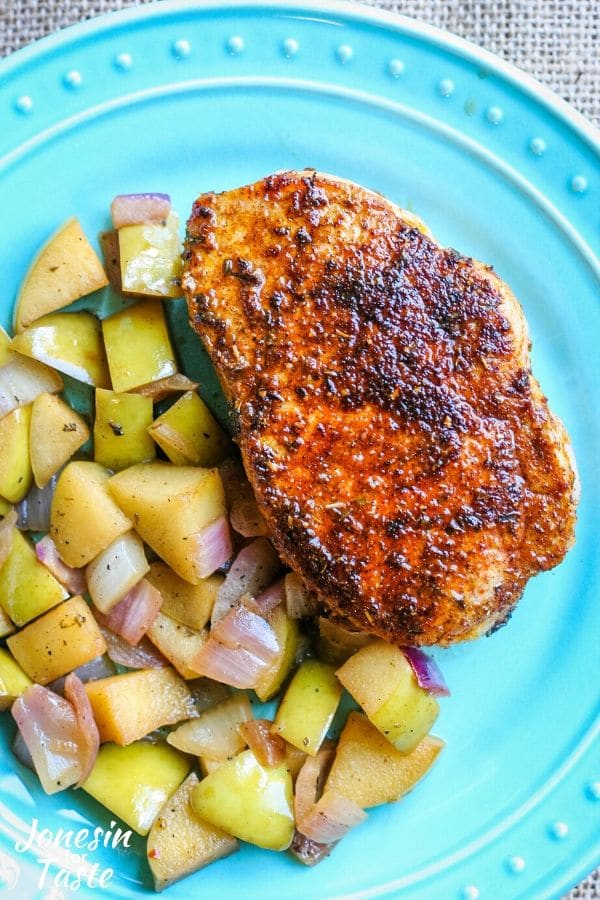 A Cajun pork chop on a blue plate next to sauteed apples and onions