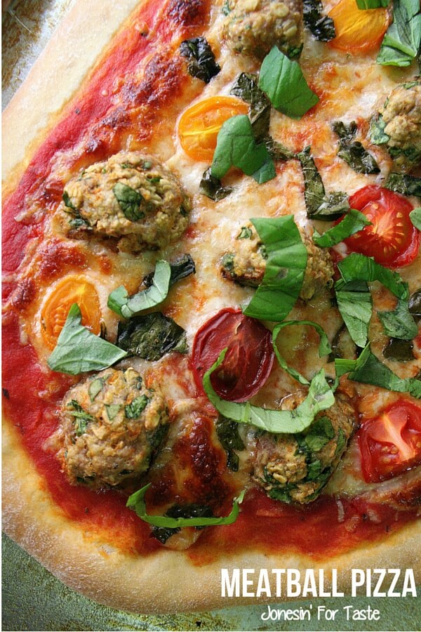 A section of pizza topped with meatballs, tomato halves, and chopped basil