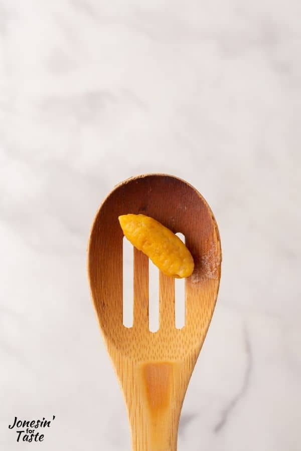 a piece of cooked pumpkin gnocchi in a wooden slotted spoon