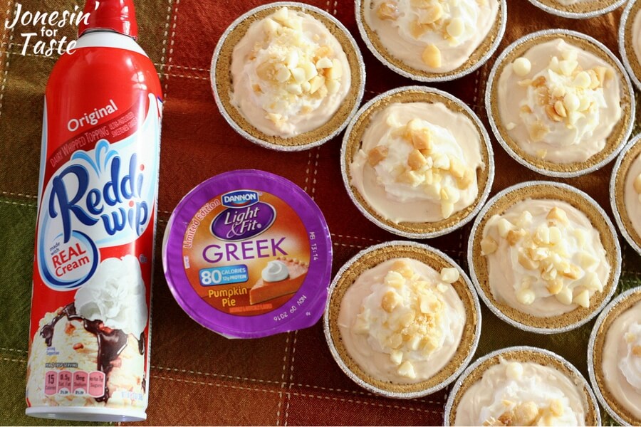 A bunch of mini no bake pumpkin cheesecakes on a tablecloth with a Reddi Wip canister and a pumpkin yogurt.