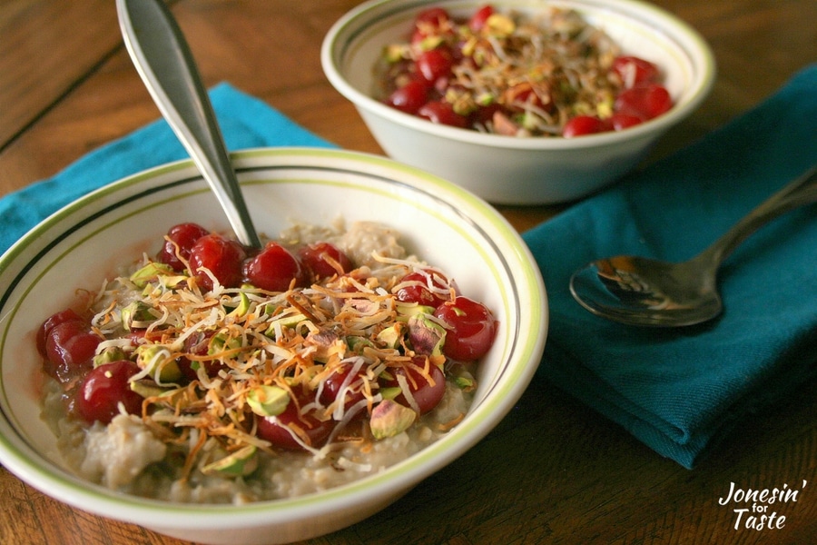 A bowl of Slow Cooker Cherry Coconut Steel Cut Oatmeal with a spoon in it in front of another bowl of oatmeal.