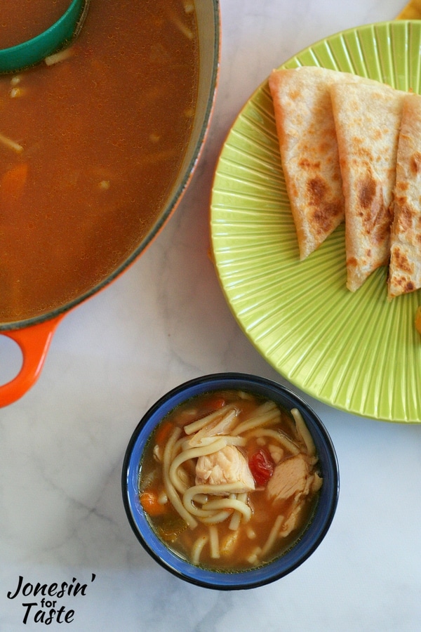 A small bowl of salsa soup next to a green plate with triangles of quesadilla and a large pot of soup next to it.