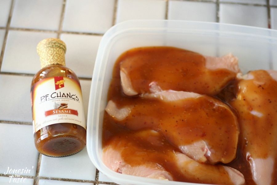 A container with chicken breasts and marinade with a bottle of marinade next to it.