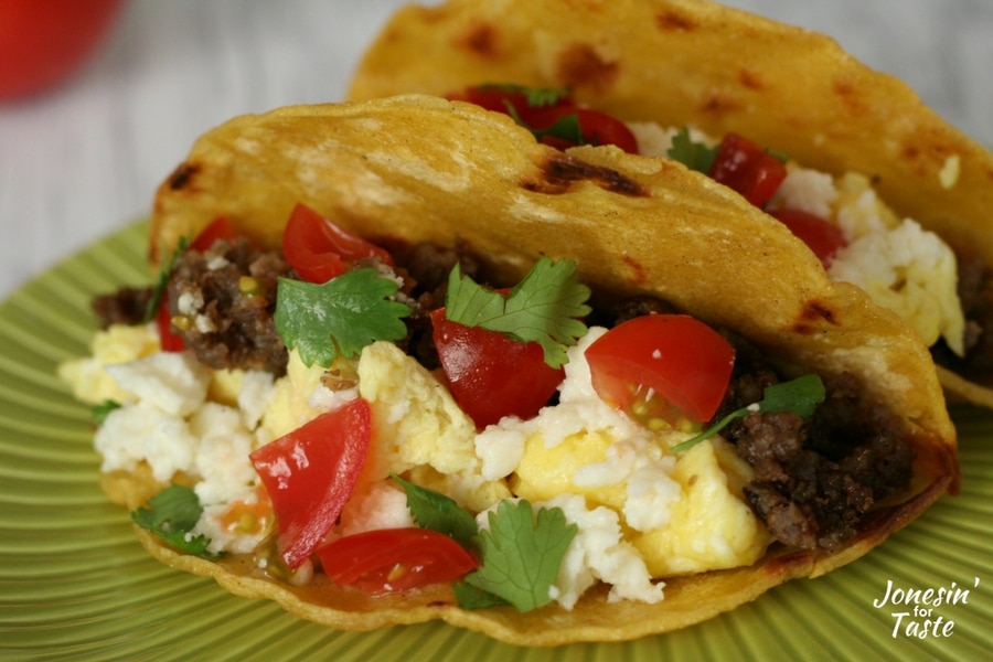 A breakfast taco made up of a corn tortilla stuffed full with ground sausage, scrambled eggs, queso fresco, diced cherry tomatoes, and cilantro.