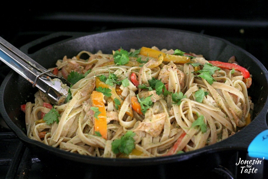 A cast iron pan of chicken fajita pasta with cilantro lime sauce garnished with cilantro leaves 