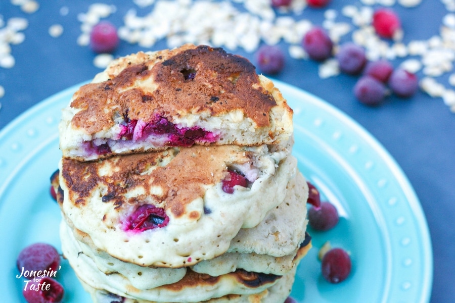 A tall stack of pancakes on a blue plate surrounded by oatmeal and frozen cranberries.