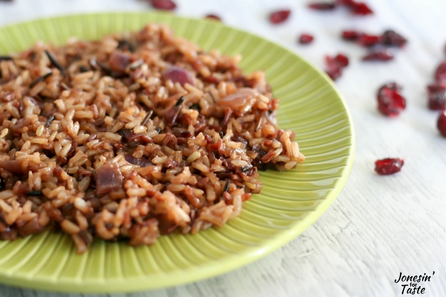 A large helping of Orange Cranberry Wild Rice on a green plate with dried cranberries in the background.