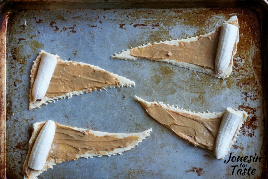 An overhead look at 4 croissant triangles topped with peanut butter and banana prepared and ready to be rolled up.