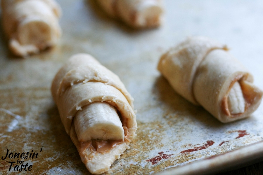 Easy Peanut Butter and Banana Croissants rolled up and on a well loved baking sheet ready to go into the oven.