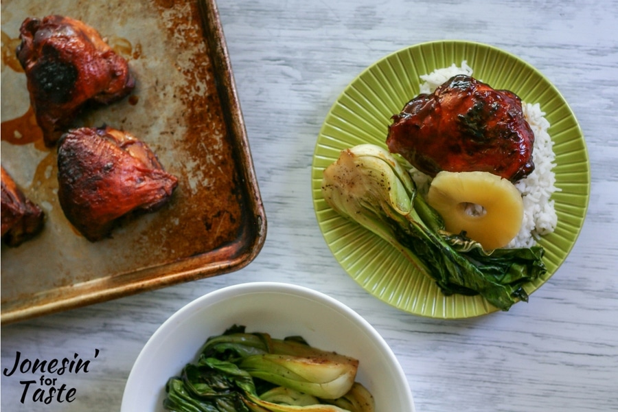 A table top view of plated slow cooker sticky pineapple chicken along with a tray of chicken and a white bowl filled with grilled baby bok choy.
