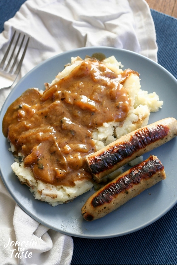 A bratwurst cut in half with mashed potatoes and onion gravy