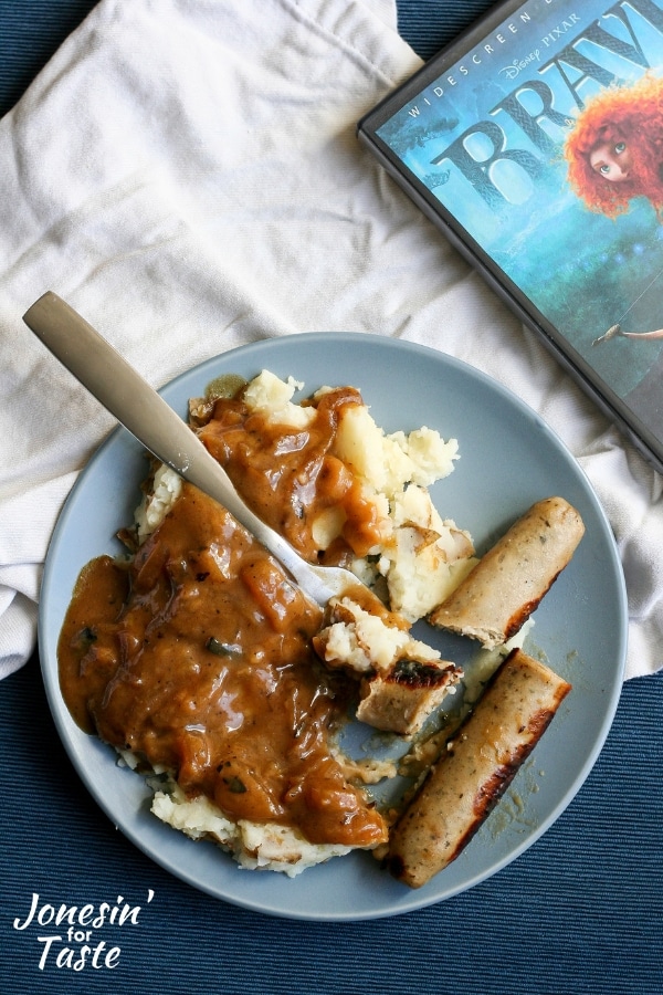 A plate of bangers and mash with a fork next to the dvd case for Brave