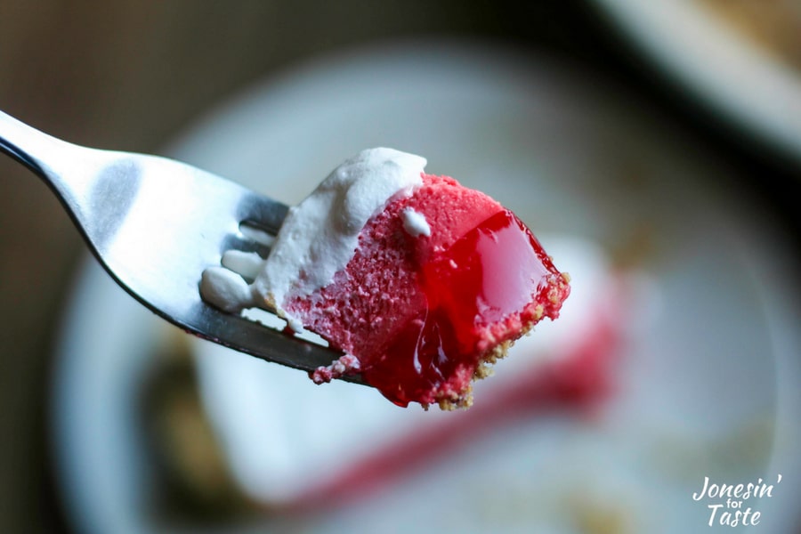 A fork full of pie showing off the three layers of pie- a jello layer with a graham cracker crust on the bottom, a pink jello & cool whip layer, with cool whip on top.