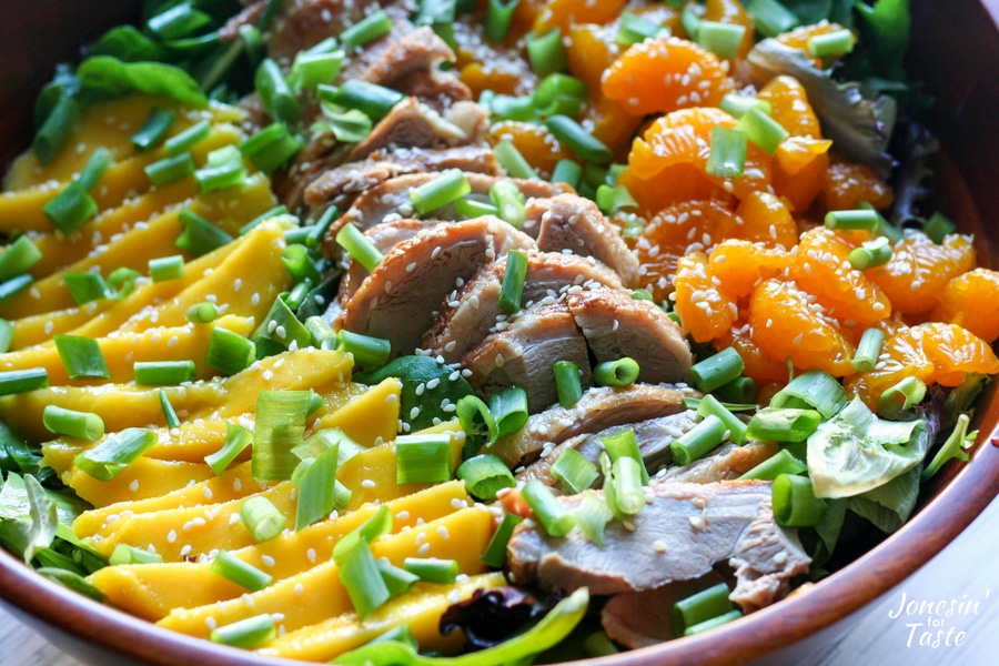 A close up of the sliced mango, roast duck, and mandarin oranges on top of the salad greens.
