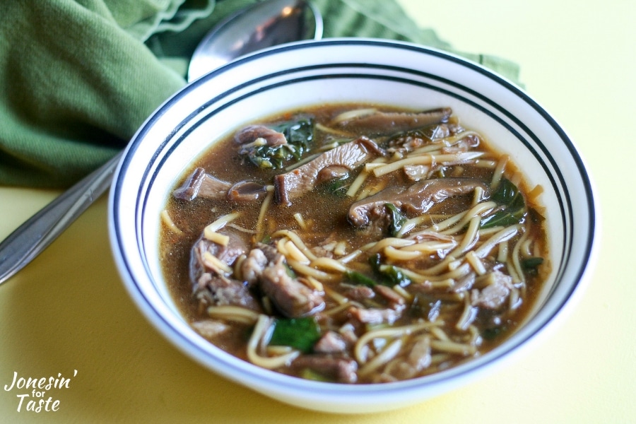 A bowl of chinese pork shoulder soup next to a spoon and green napkin