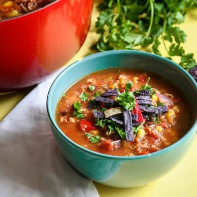 A bowl of tortilla soup next to a white napkin and cilantro bunch