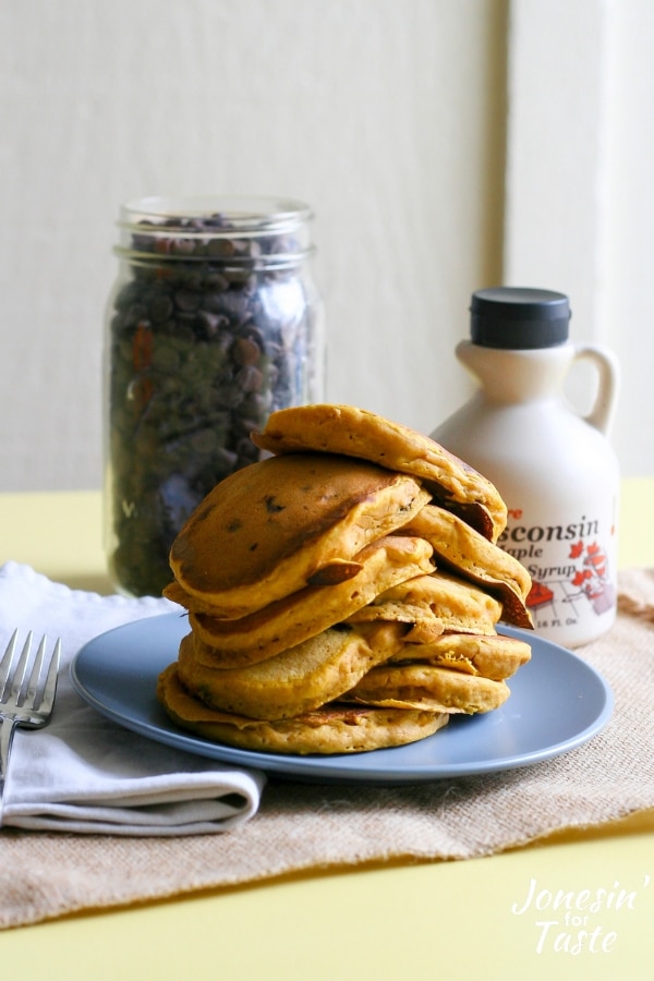 Pumpkin pancakes next to a bottle of maple syrup and a jar of chocolate chips