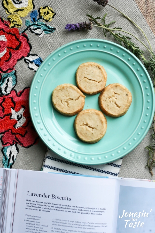 Lavender cookies on a plate next to an open cookbook.