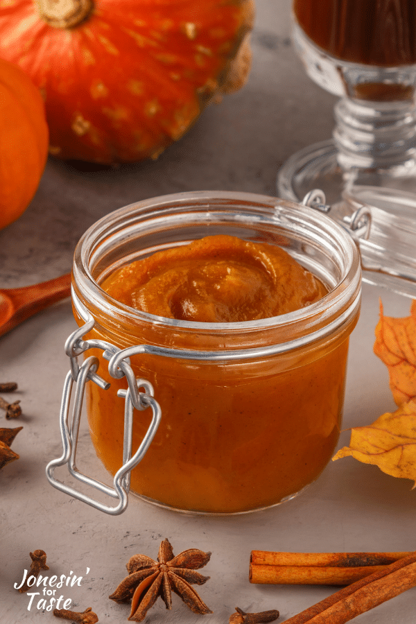 a jar of homemade canned pumpkin surrounded by different fall items like leaves, pumpkins and fall spices