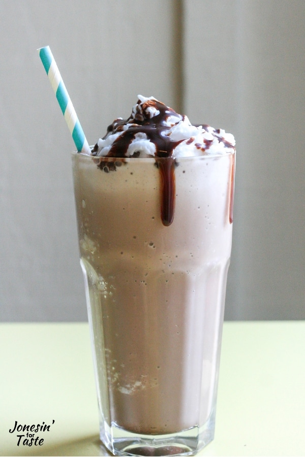 A glass full of frozen hot chocolate topped with whipped cream and chocolate syrup,
