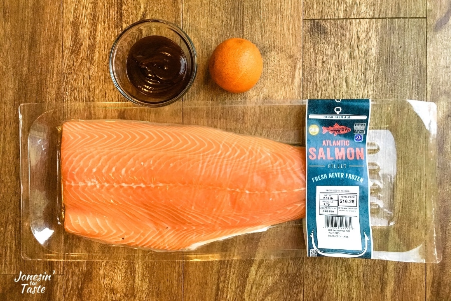 uncooked salmon, an orange. and barbecue sauce on a wooden table