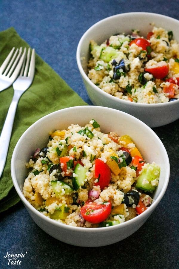 two bowls of couscous salad next to a green napkin with 2 forks
