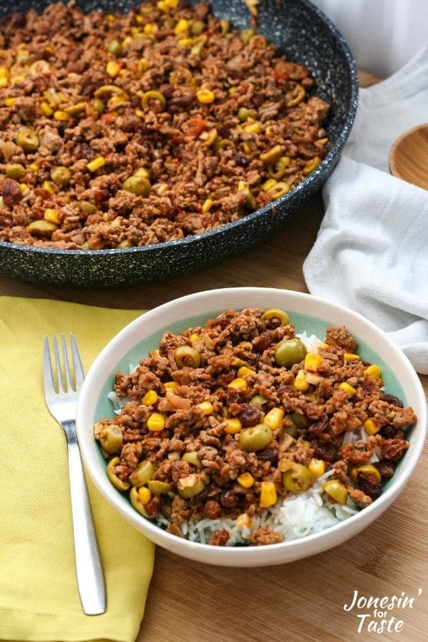 a bowl of picadillo served over rice next to a skillet and fork