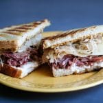 a corned beef and sauerkraut sandwich halved and sitting on a yellow plate