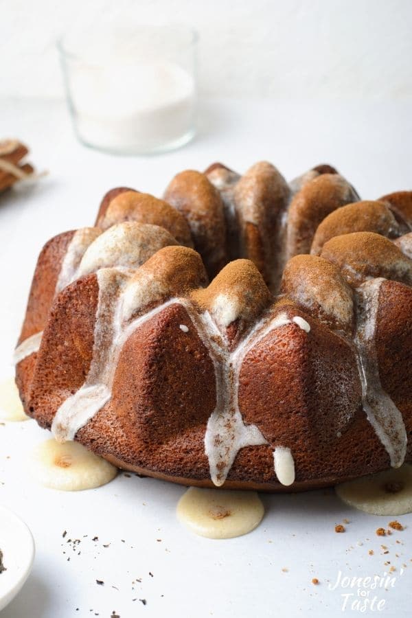 a dark brown bundt cake with ribbons of white glaze dripping down the crevices and a light dusting of cinnamon on top