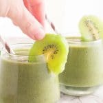 a person places a kiwi slice onto the rim of a cup full of smoothie