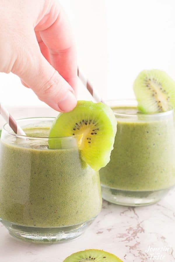 a person places a kiwi slice onto the rim of a cup full of smoothie