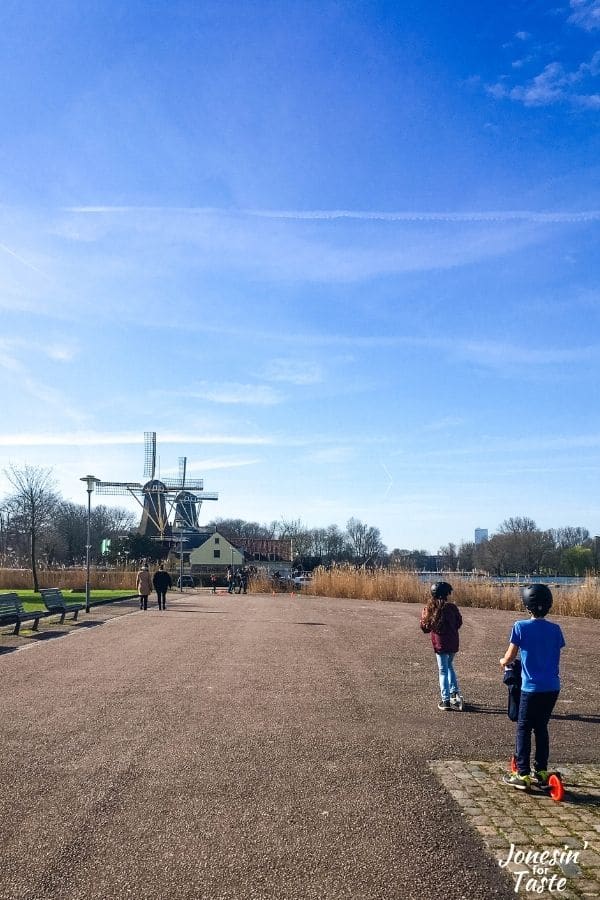 two children ride scooters towards a pair of windmills