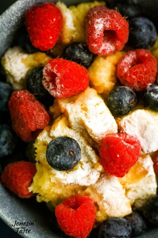 a close up view of bread pudding topped with blueberries and raspberries and a light dusting of powdered sugar