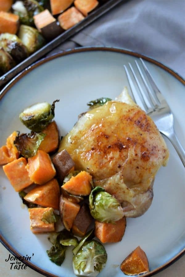 a chicken thigh and roasted Brussles sprouts and sweet potatoes on a white plate with a fork