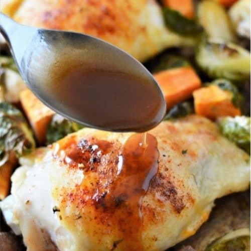 a spoon pouring maple balsamic glaze over a piece of cooked chicken thighs surrounded by sweet potato and brussel sprouts