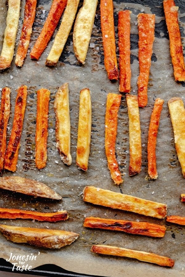 baked carrot and potato fries mixed together in rows on a cookie sheet