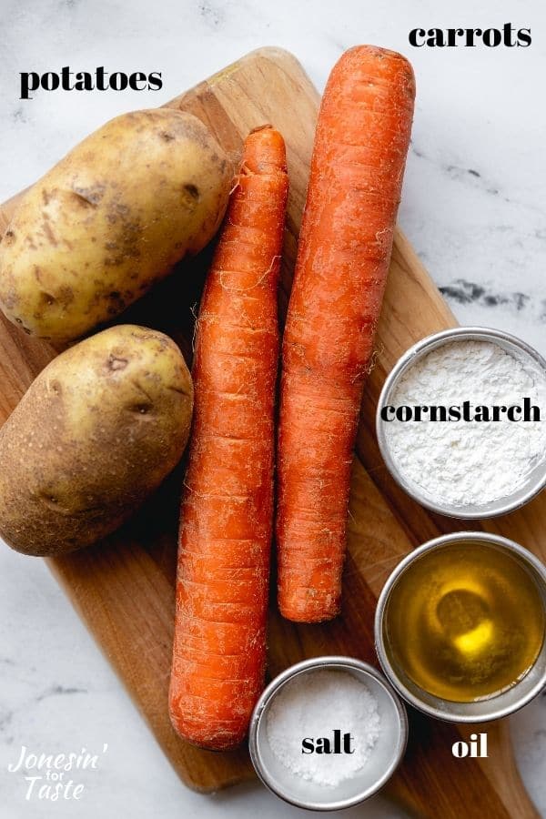 potatoes, carrots, and bowls of cornstarch, oil, and salt on a small wooden cutting board on a marble counter