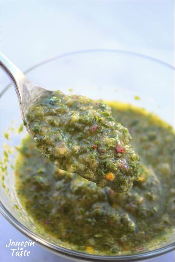 a spoon lifting out a spoonful of chimichurri from a glass bowl