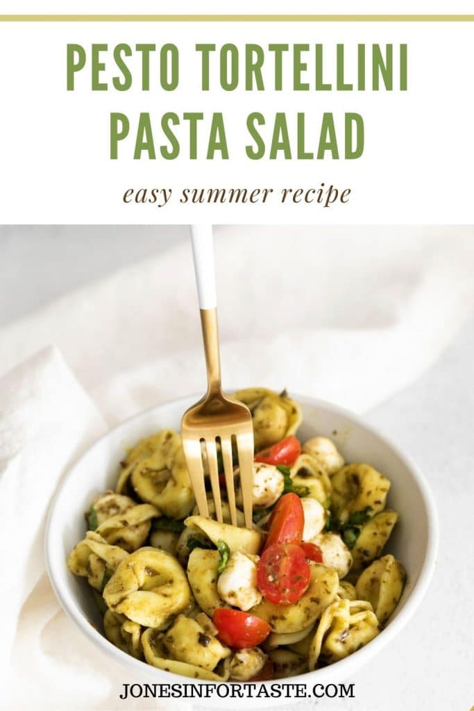 a hand holding a fork. The fork is pressing down on a tortellini in a white bowl to pick up. Text above the photo says pesto tortellini pasta salad, easy summer recipe.