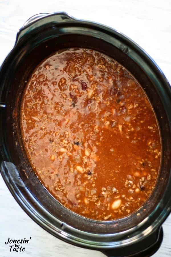 a reddish brown liquid in a slow cooker liner with beans and meat floating in it